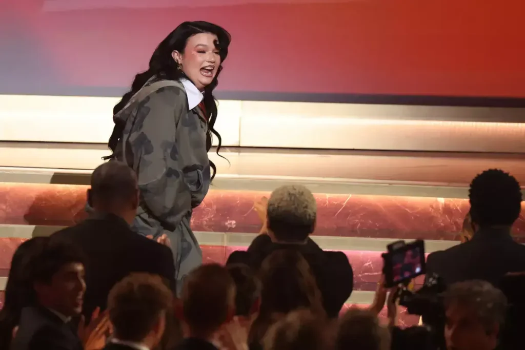 Lola Young glimlacht verrast terwijl ze het Grammy-podium op loopt om haar prijs voor beste solo-popnummer in ontvangst te nemen